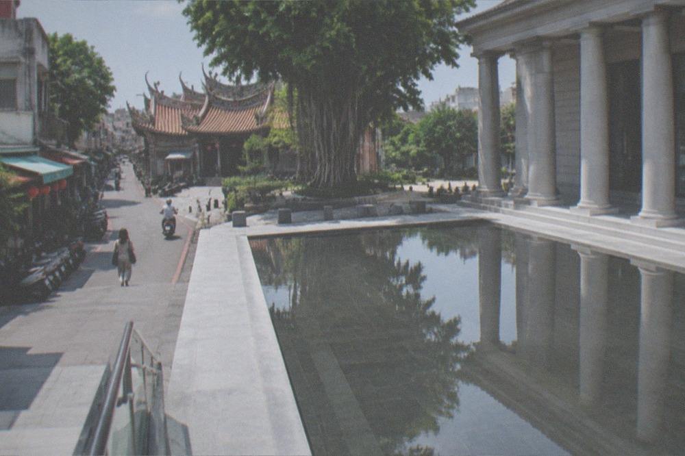 A classical style museum building with a columned facade reflected in a wide ornamental pool