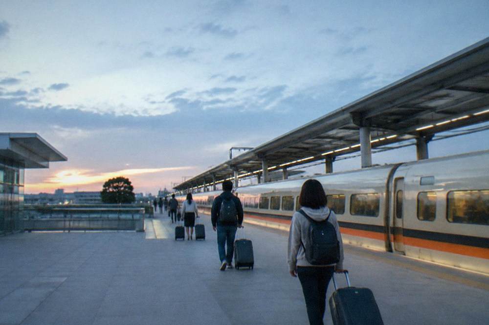 A modern high speed rail station platform with a train waiting and travelers with rolling bags