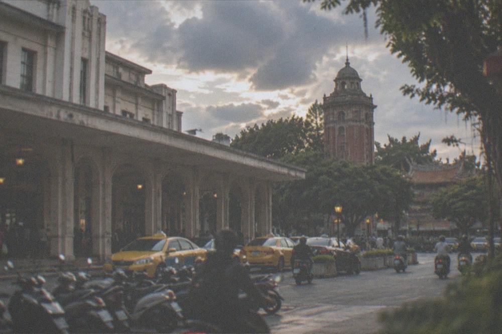 A red-brick historic tower surrounded by trees in a city plaza at dusk