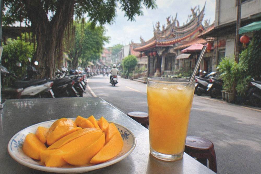 Fresh mango slices arranged on a plate beside a glass of iced mango drink