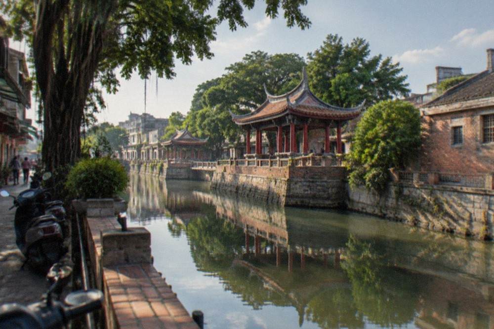 A canal in Tainan reflecting old brick warehouses and green trees