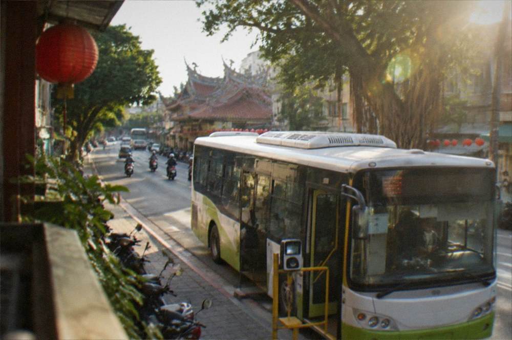 A Tainan city bus at a stop on a sunny street with a card reader at the front