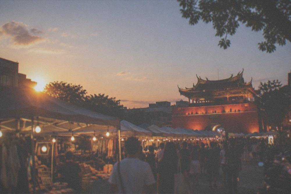 An illuminated historic Chinese gate tower at night, with warm floodlighting on red walls and a lit courtyard