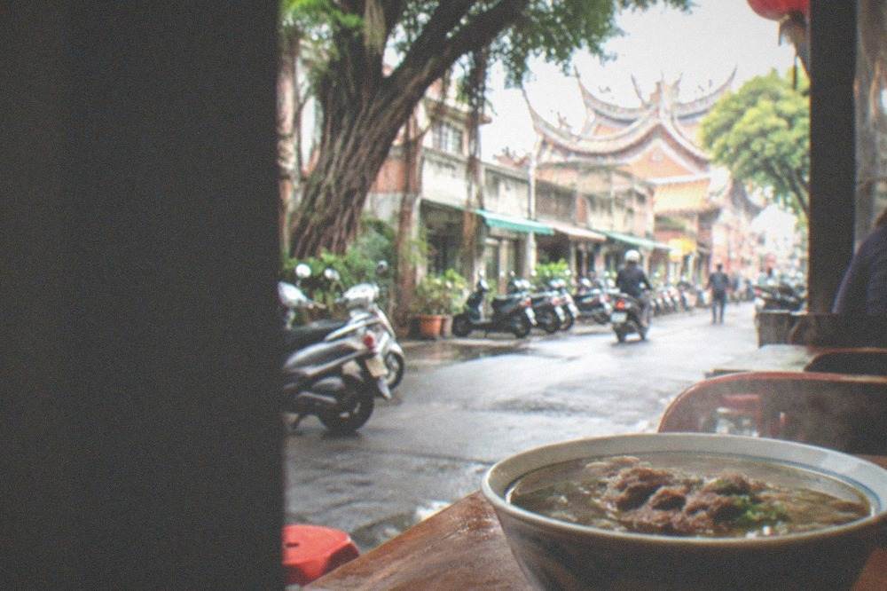 A steaming bowl of Tainan beef soup on a wooden table in a small shop