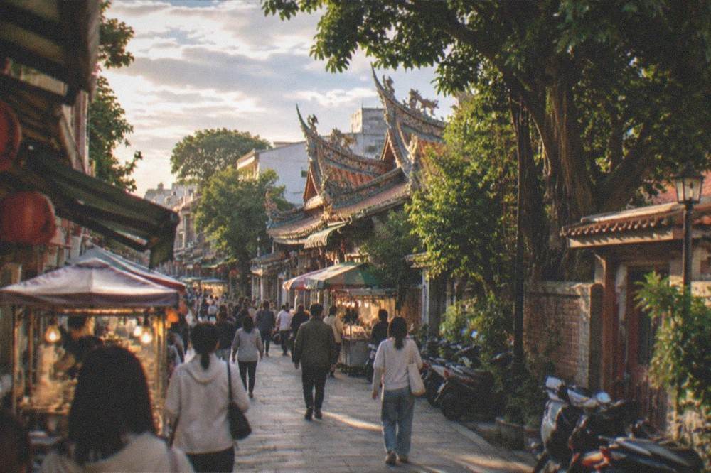 People in light jackets walking through a dry, warm Tainan evening market in autumn