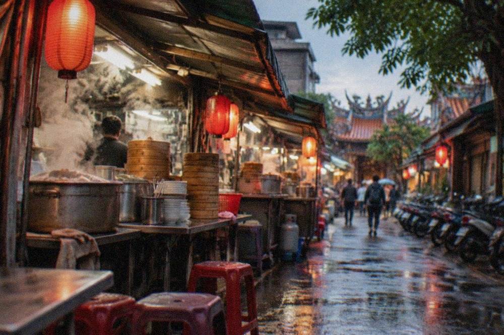 A small Tainan eatery at dusk with steam rising from soup pots and lanterns glowing along the street