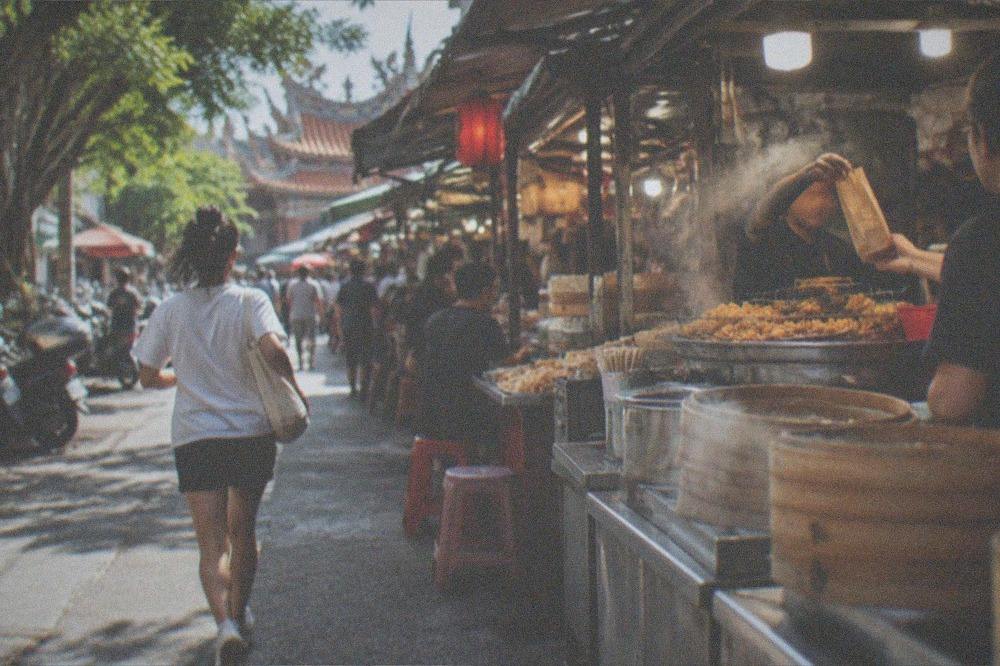 A vendor handing a paper bag of fried snacks across a crowded Tainan stall counter at night
