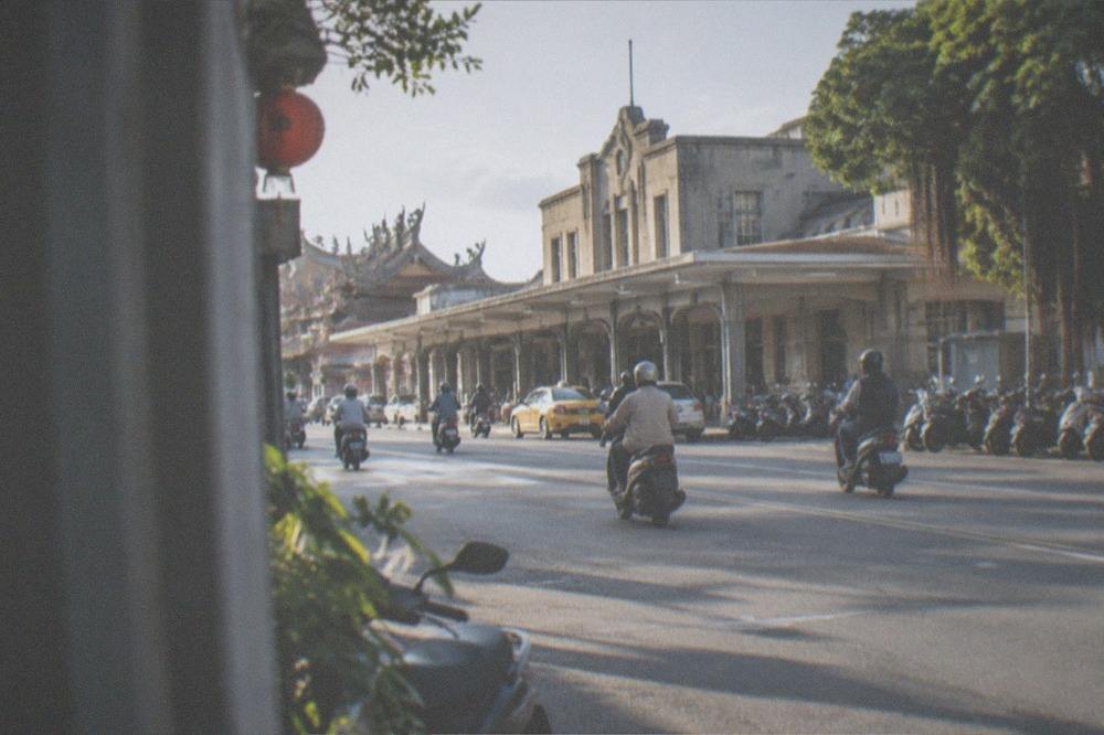 A wide flat Tainan road with scooters in traffic under a sunny sky