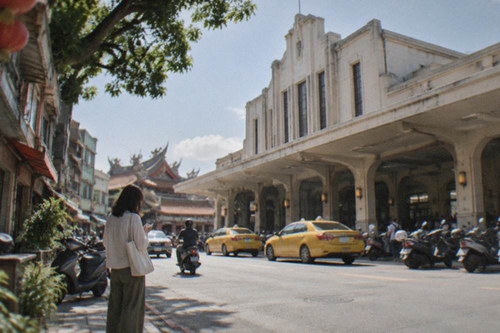 A traveler checking a phone on a sunlit Tainan street lined with old shopfronts