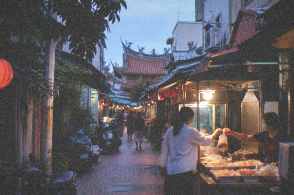 A vendor handing a bag of snacks to a customer across a night market stall counter
