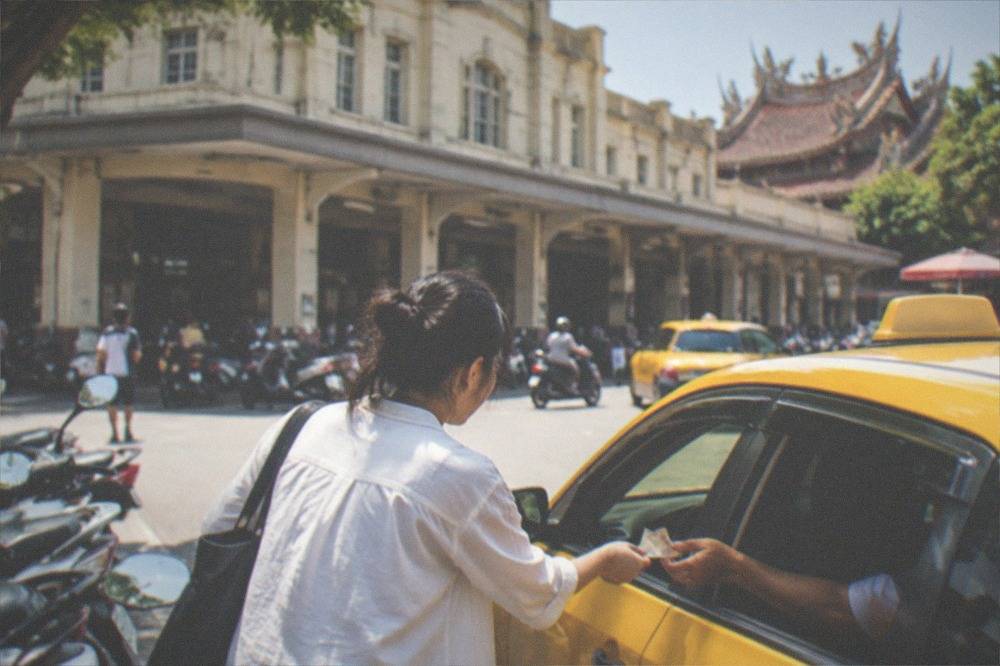 A passenger paying a taxi driver with cash through an open car window