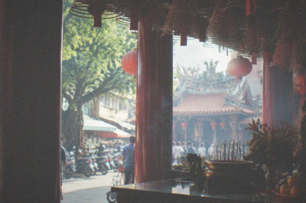 Ornate temple interior with red pillars, hanging lanterns and an altar with offerings