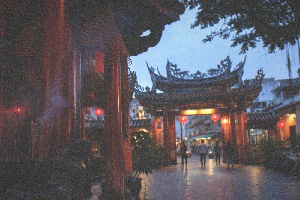 Illuminated temple gateway at dusk with stone courtyard and lantern light