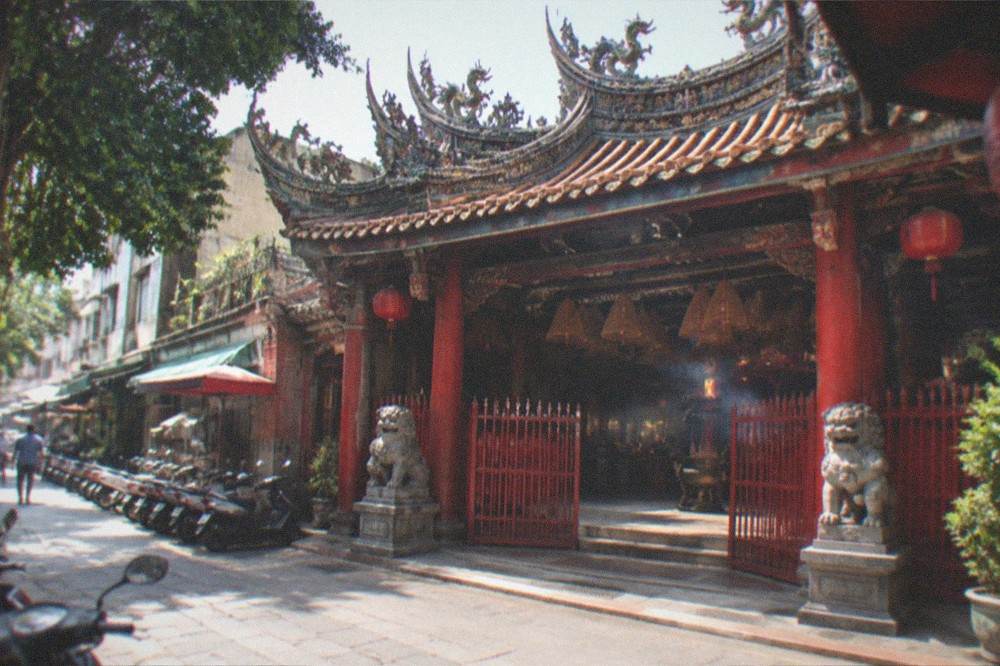 A wide view of a Taiwanese temple facade with red gates and stone lions at the entrance