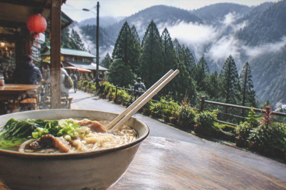 A bowl of steaming noodles on a wooden table at a food stall