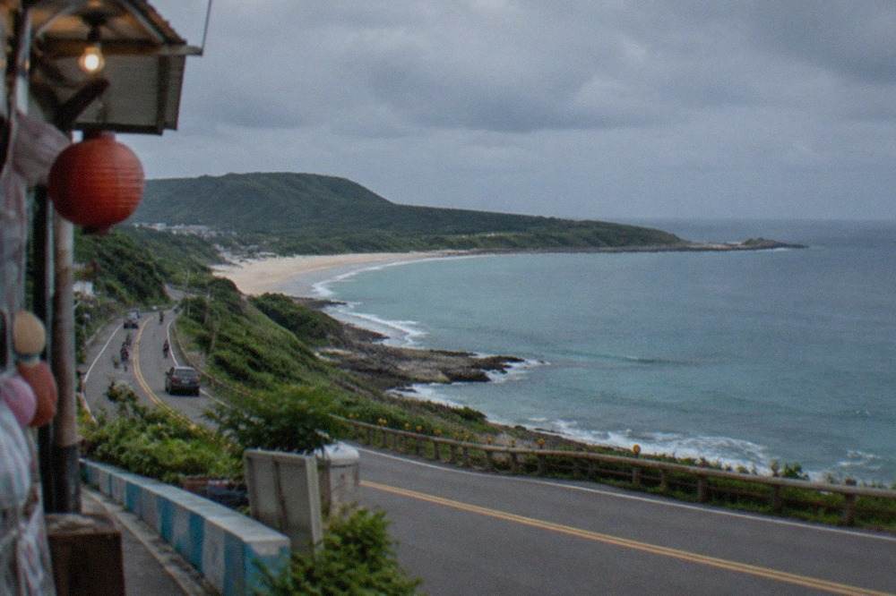 A coastal highway curving along a green peninsula with blue sea on the horizon