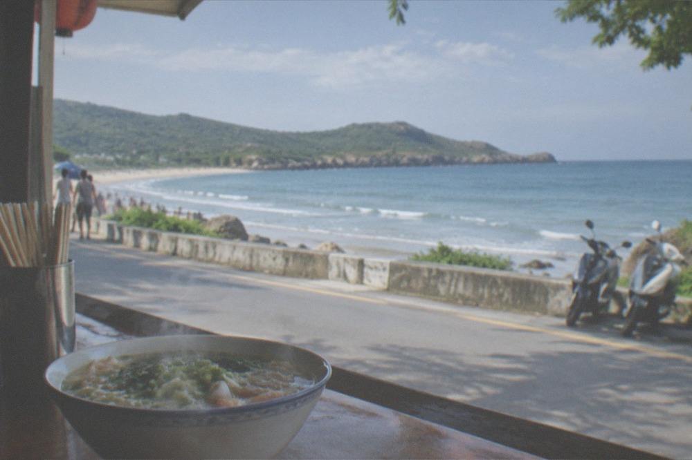 A bowl of steaming noodle soup on a wooden stall counter beside chopsticks