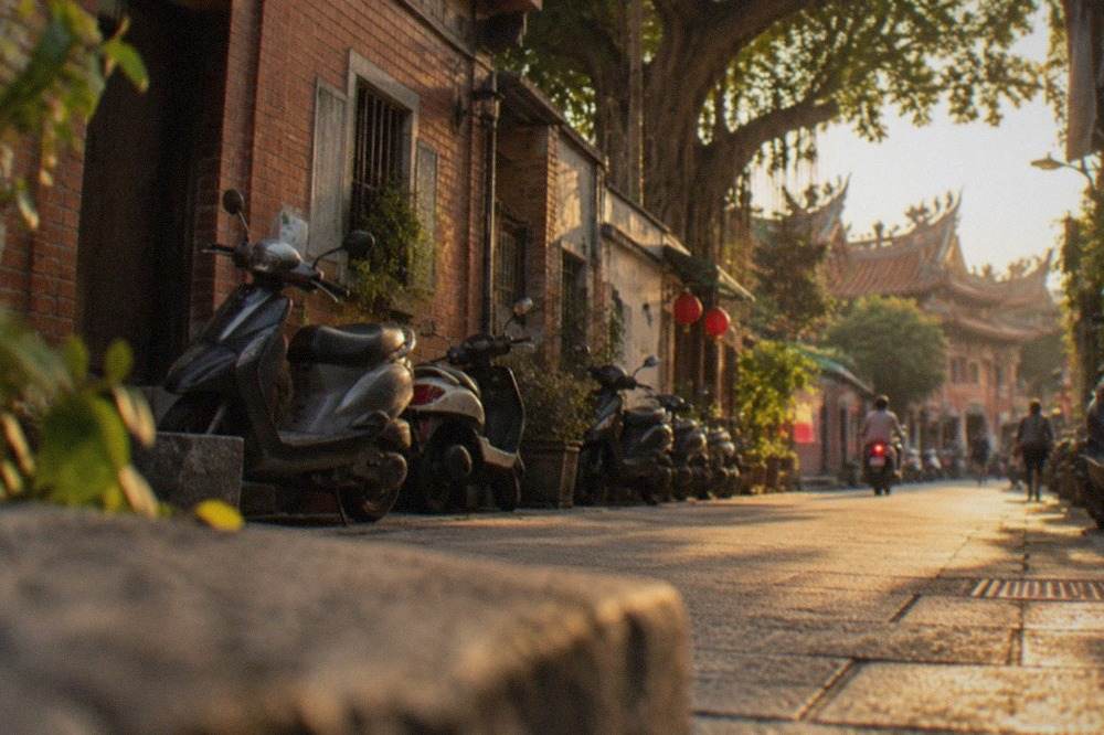 A narrow old street in Tainan lined with low brick buildings and scooters parked along the wall