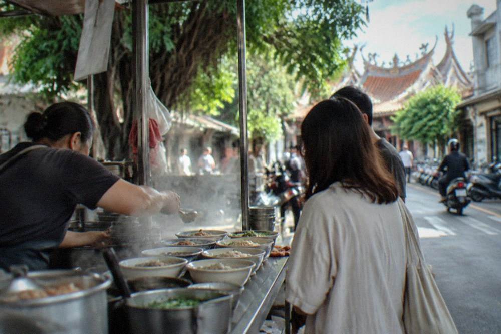 A food stall counter in Tainan with steaming bowls lined up and a vendor serving customers