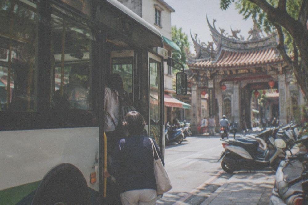 A city bus stopped at a curb in Tainan with passengers boarding near a temple gateway
