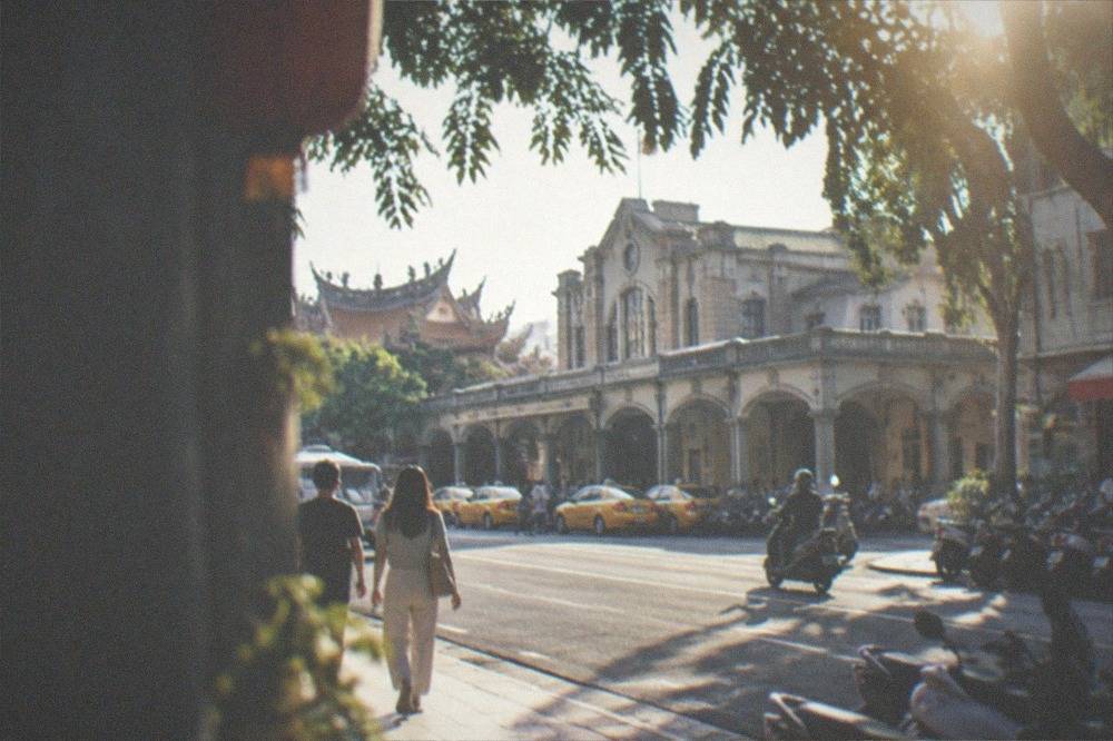 Visitors walking a wide Tainan boulevard under strong midday sun