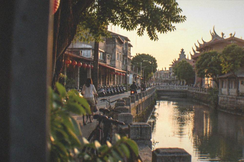 A canal-side street in Tainan at golden hour with old low buildings and bicycles