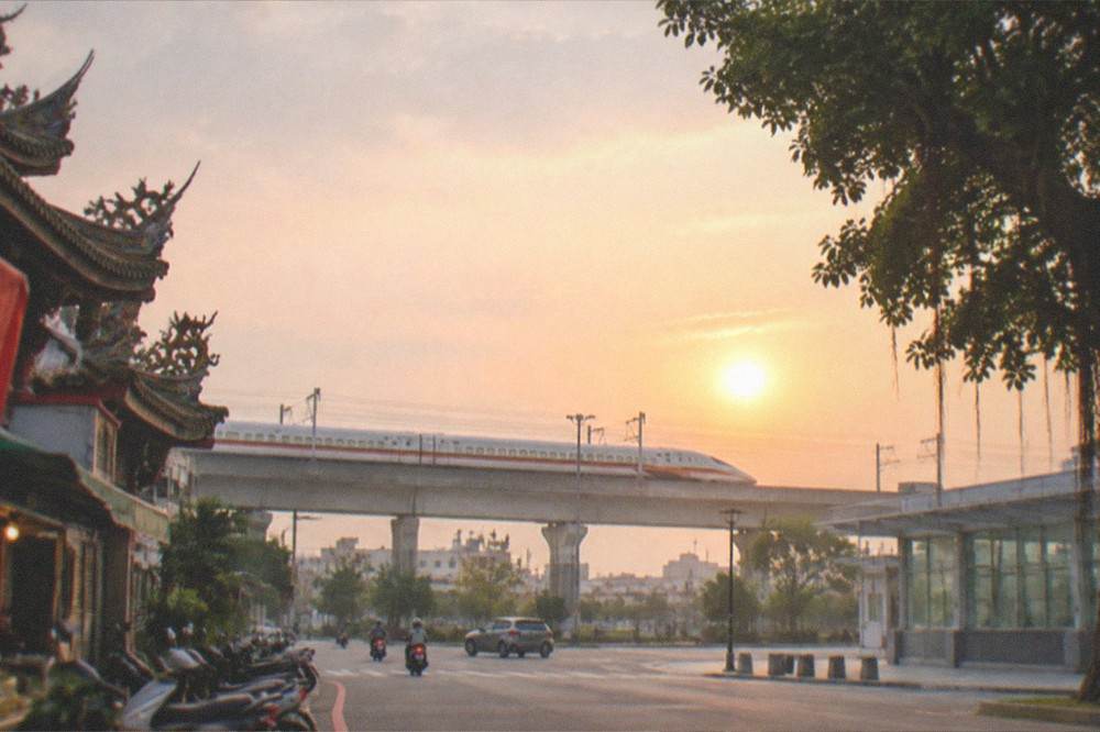 A high speed rail train traveling across an elevated viaduct at sunset