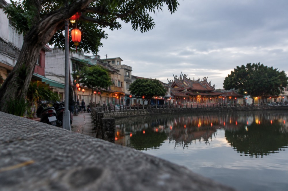 Lantern installations reflected in still harbor water at dusk