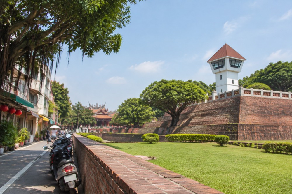 Red-brick walls of Anping Old Fort with a green lawn and a white lookout tower under a blue sky