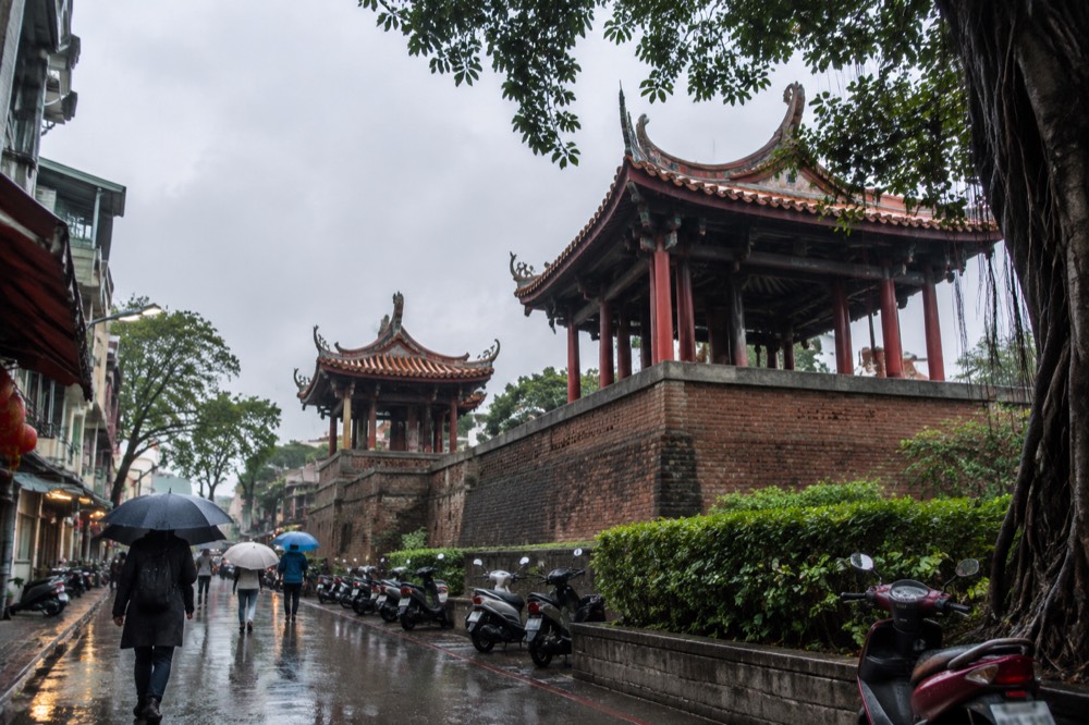 Rain falling on a wet street with closed umbrellas and reflective pavement