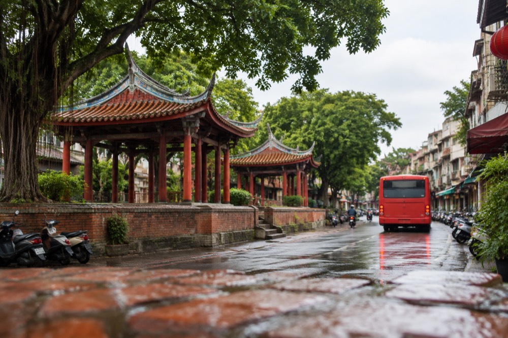 A red city bus pulling away from a stop on a Tainan street