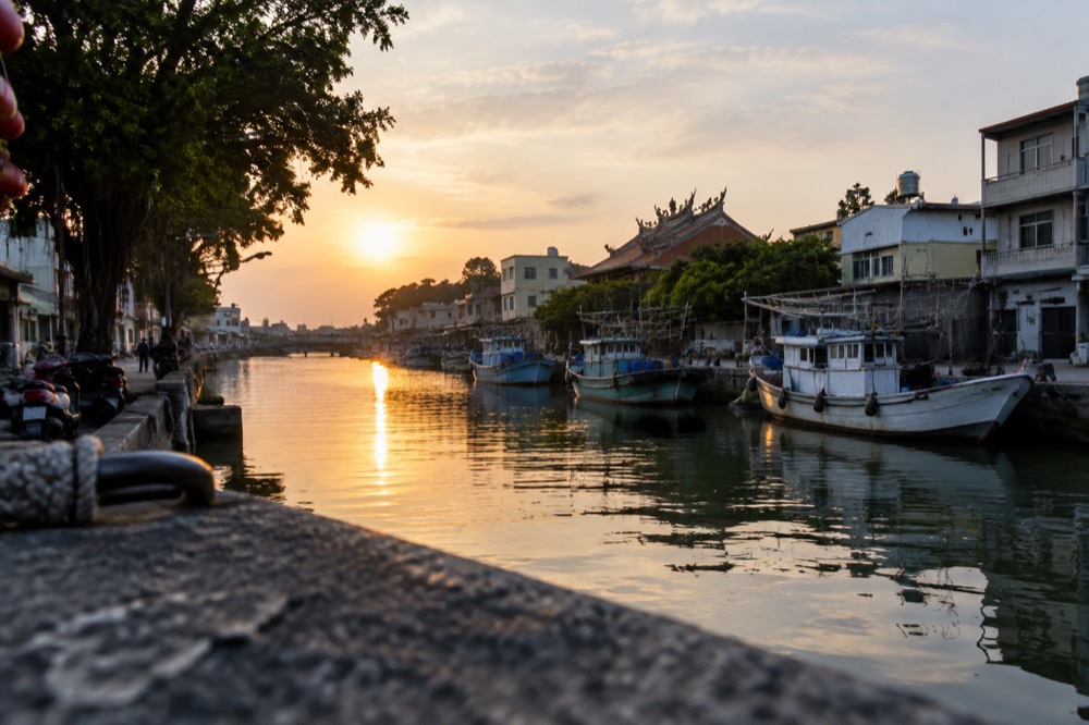 Sunset over the Anping canal with boats moored along the bank