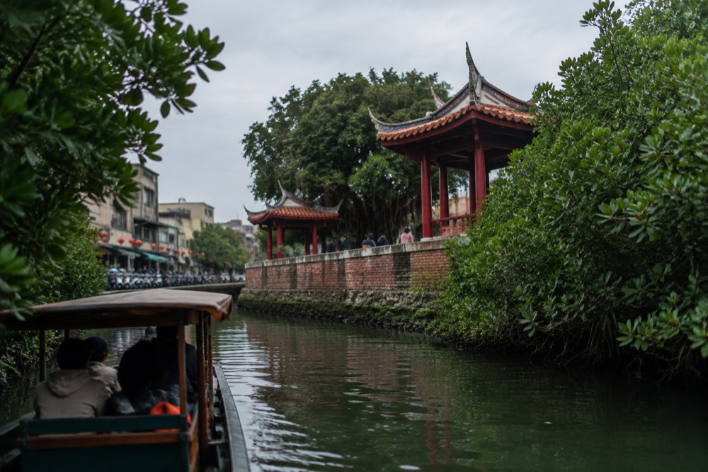 A canal boat gliding between dense green mangrove branches forming a leafy tunnel