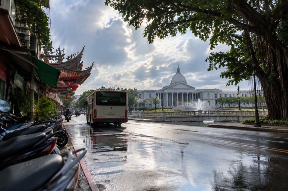 A city bus pulling away from a stop on a rain-wet Tainan road