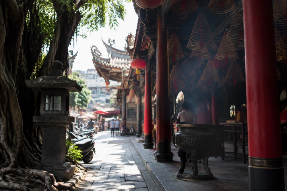Stone lanterns and banyan tree roots beside a temple pathway in Tainan