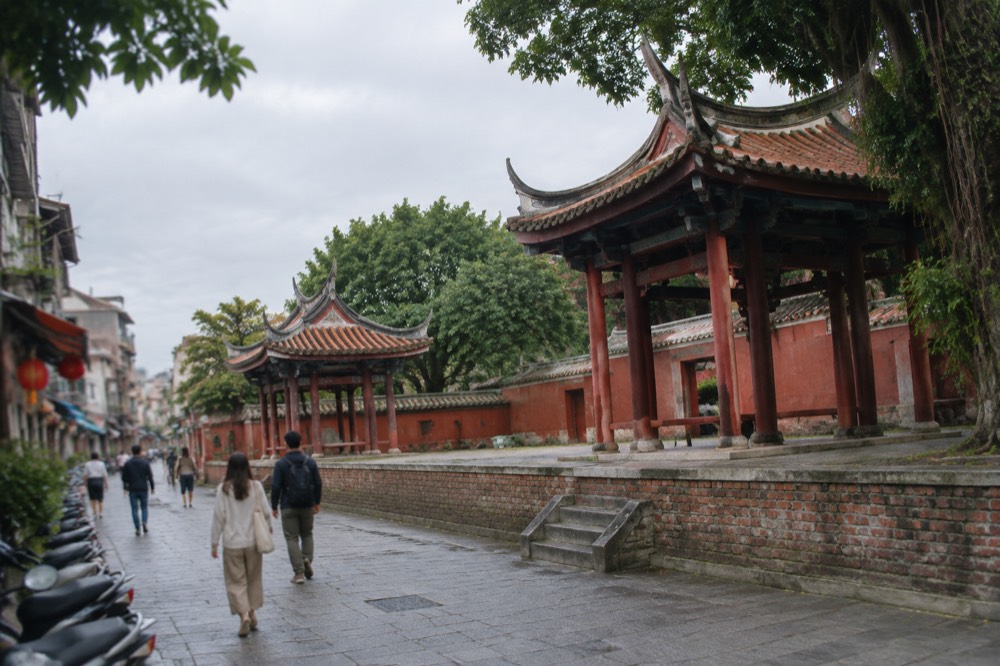 Visitors walking past the red walls of a historic Tainan temple in warm afternoon light