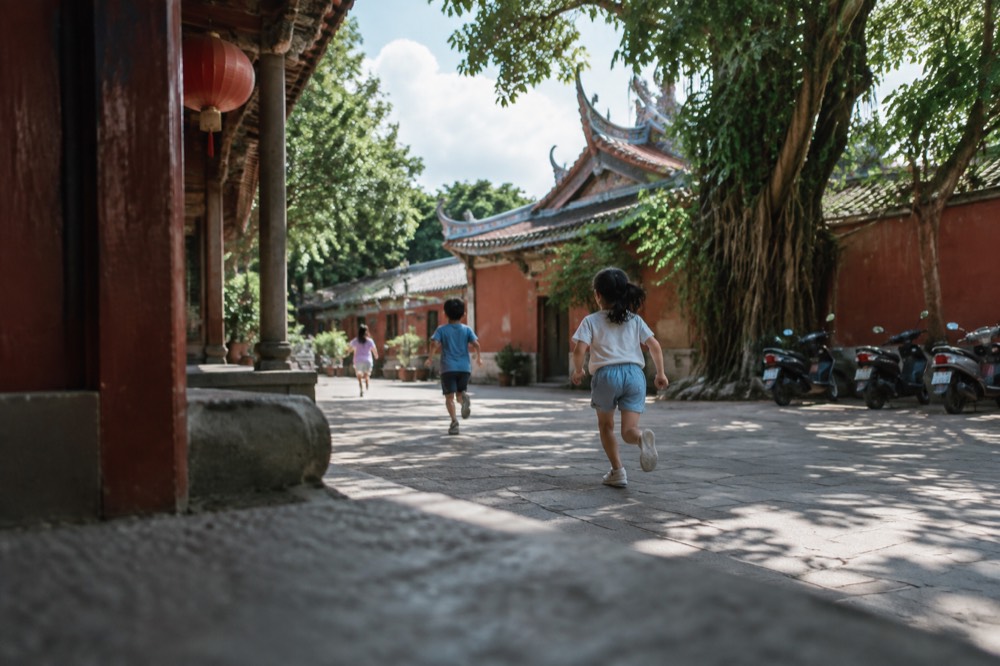 Children running across a shaded temple courtyard in Tainan with red walls and old trees