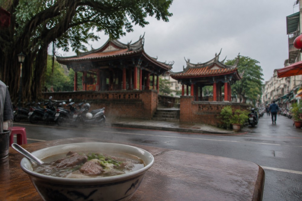 Bowl of steaming beef soup on a wooden table in a small Tainan eatery