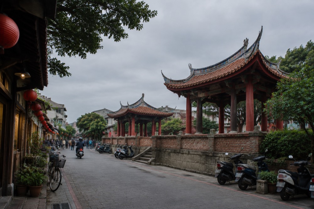 A narrow old street with low wooden-fronted buildings, lanterns and a bicycle in Tainan