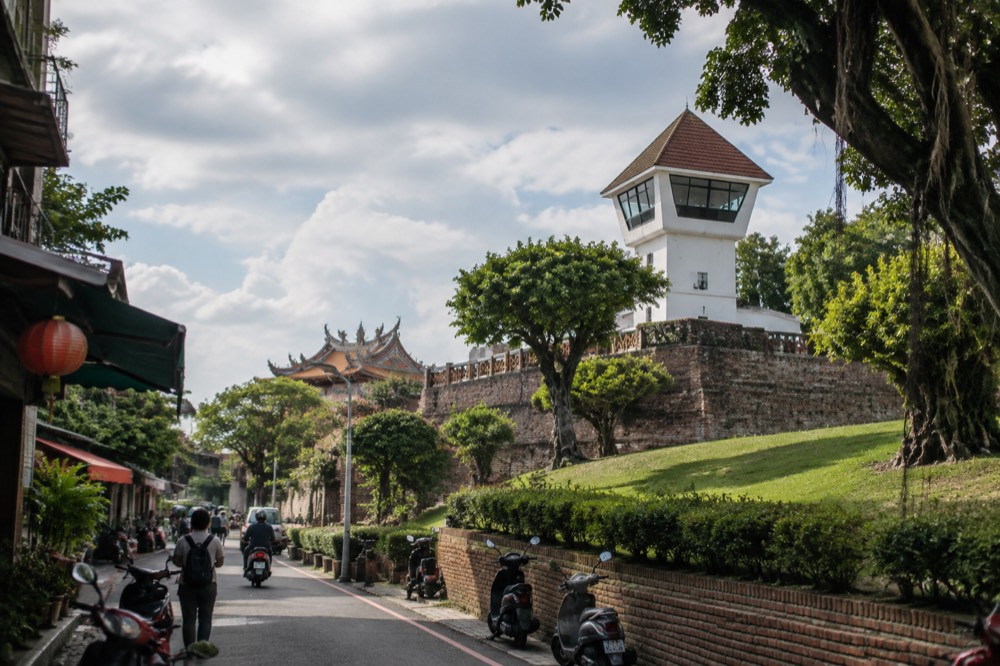 A whitewashed fort lookout tower on grassy lawns beside old brick ramparts in Anping