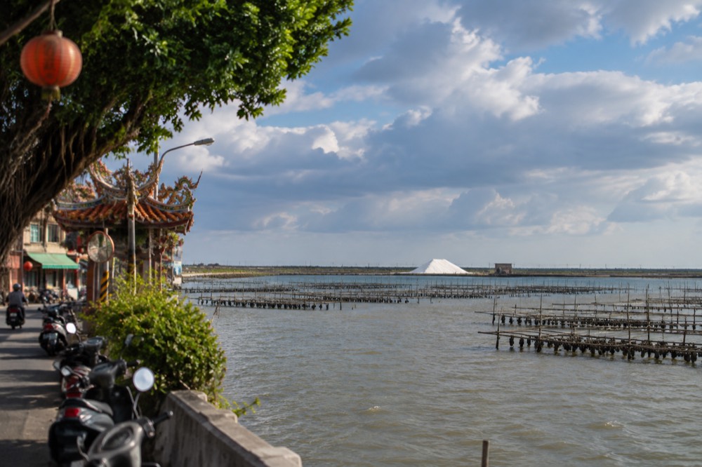 A white salt mound under a wide sky beside lagoon wetlands on Taiwan's southwest coast
